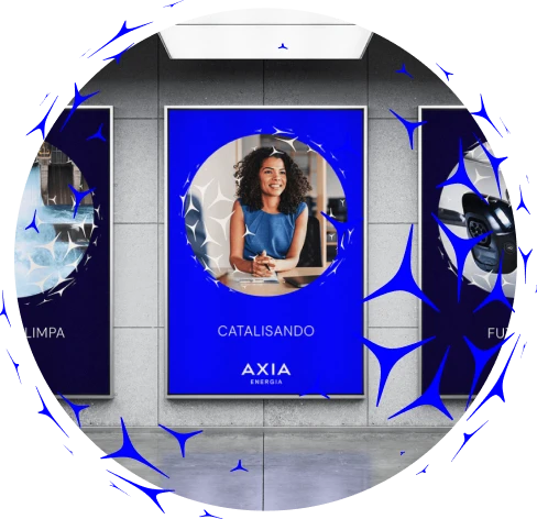 Painéis digitais em uma parede moderna, com destaque para um cartaz azul central mostrando uma pessoa sentada à mesa; texto ‘Catalisando – AXIA Energia’, com elementos gráficos azuis ao redor.
