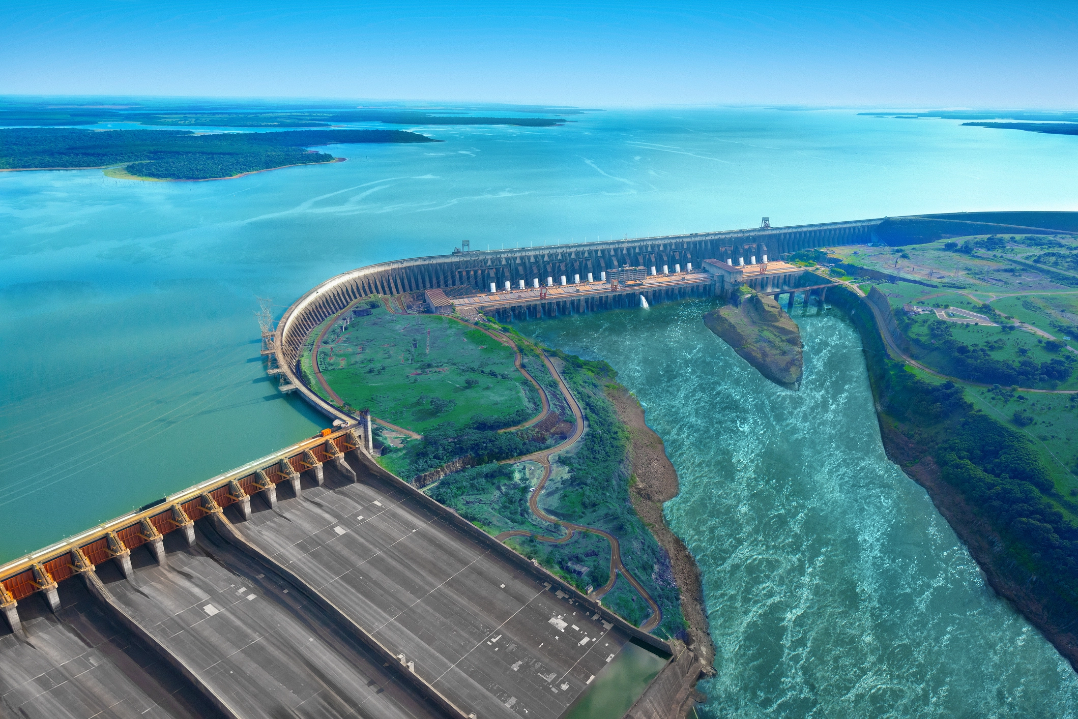 Aerial view of a large hydroelectric power plant with dam, reservoir, and spillway, surrounded by water and green areas.