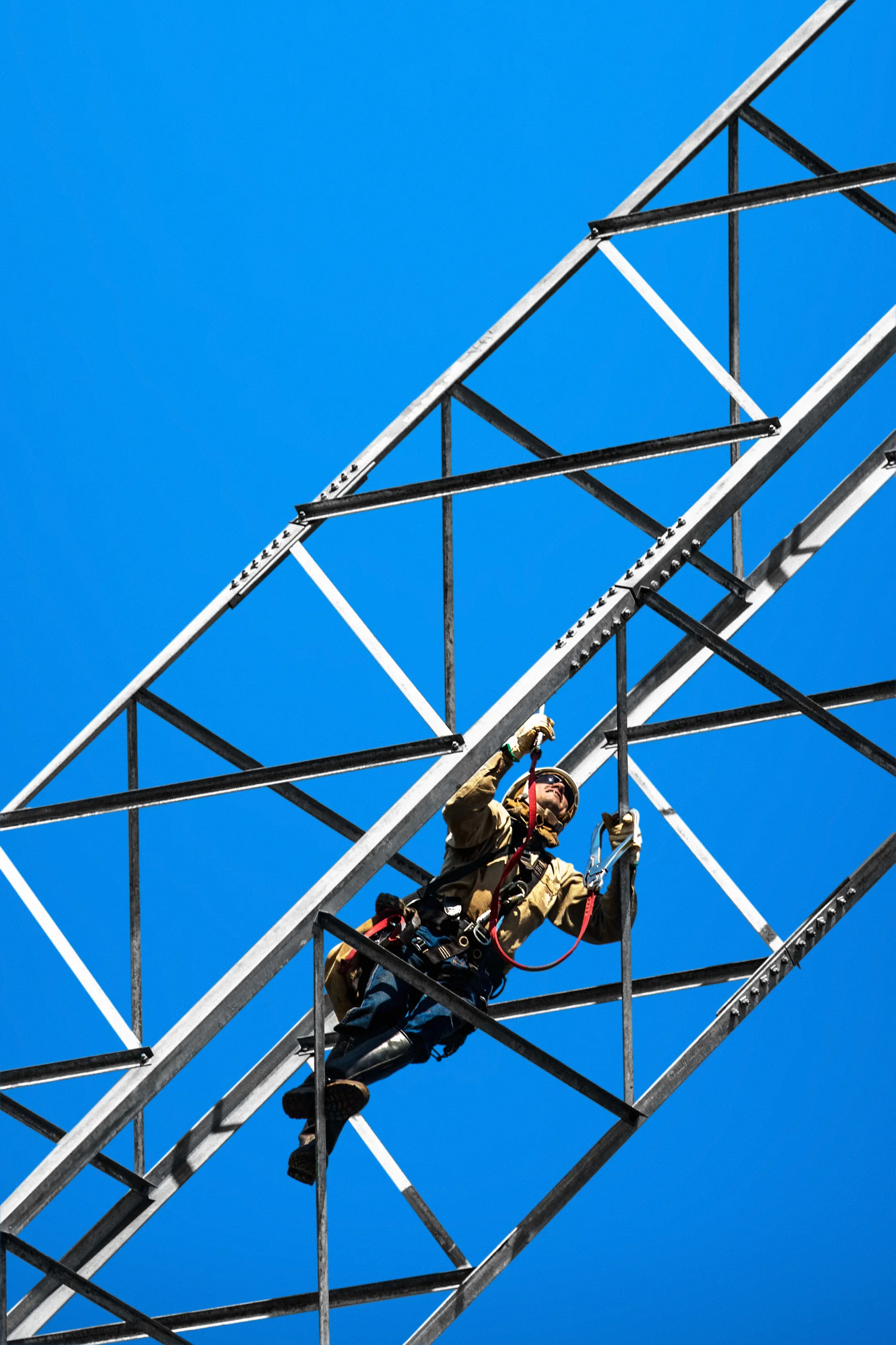 Trabalhador com equipamentos de segurança escala uma torre de metal contra um céu azul claro.