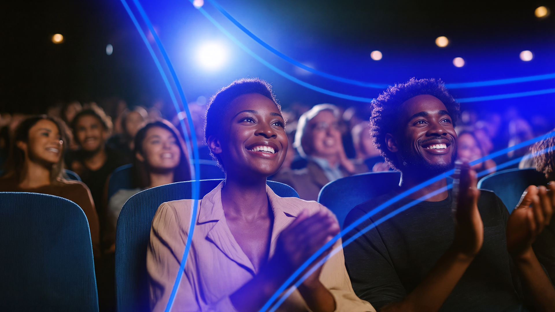 Homem e mulher negros sorriem e apludem em plateia de teatro
